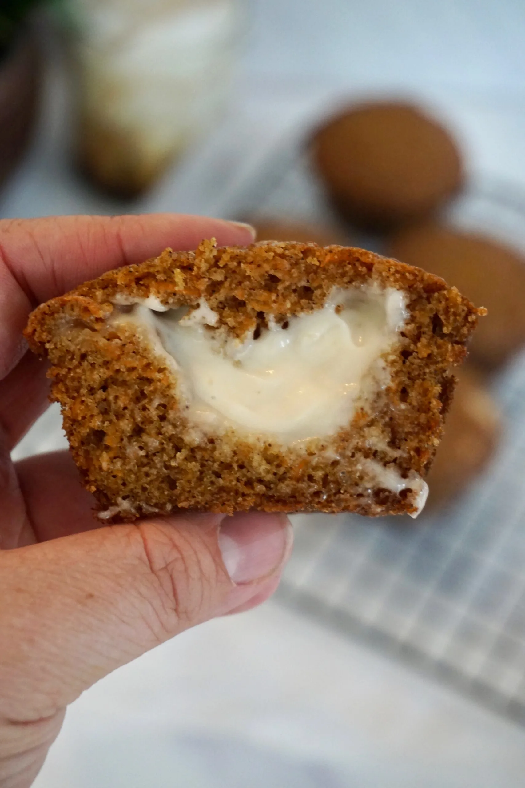 carrot cake muffin with maple cream cheese frosting in the middle held in a woman's hand