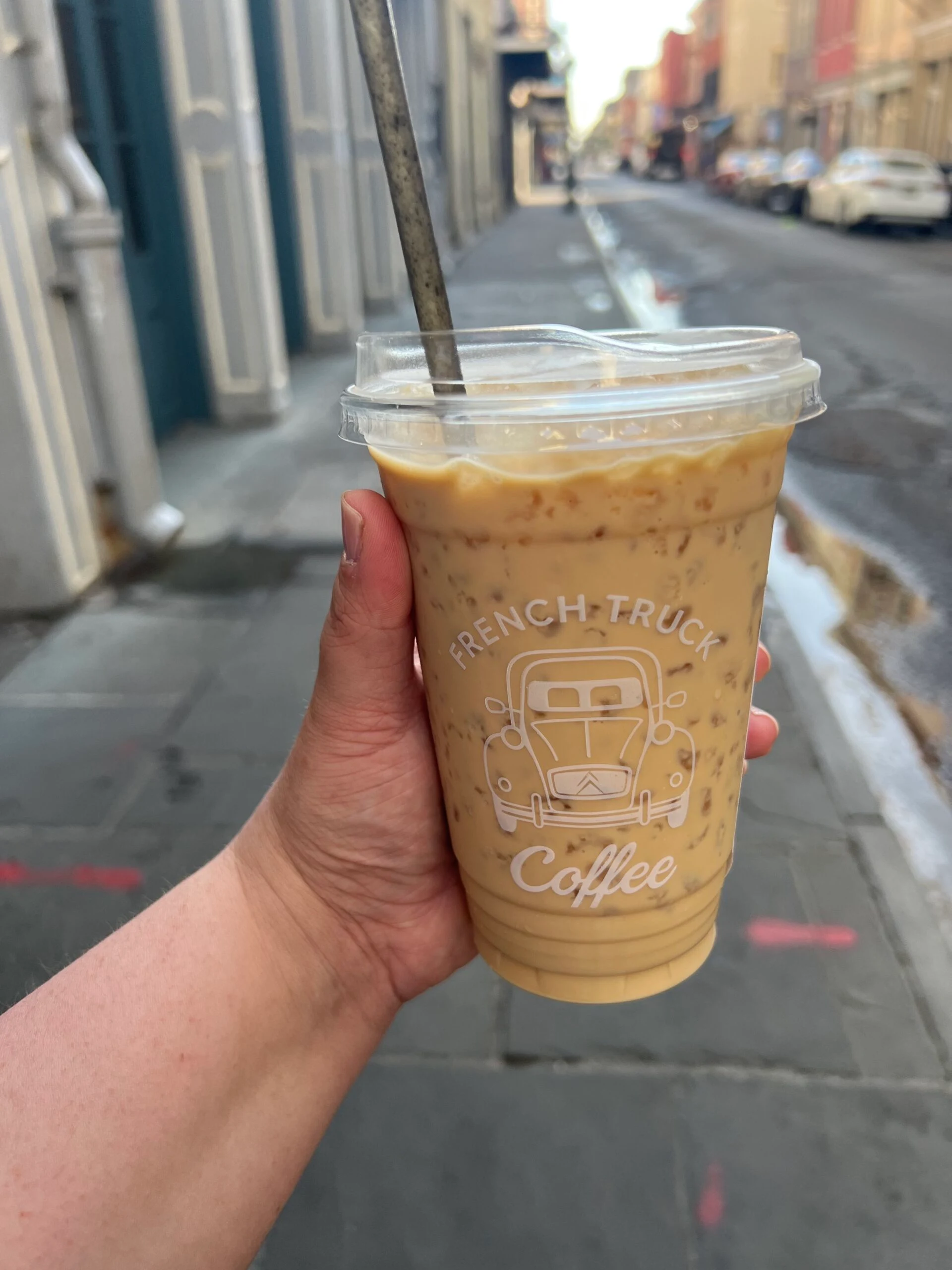 Iced latte in a woman's hand held in front of a city street