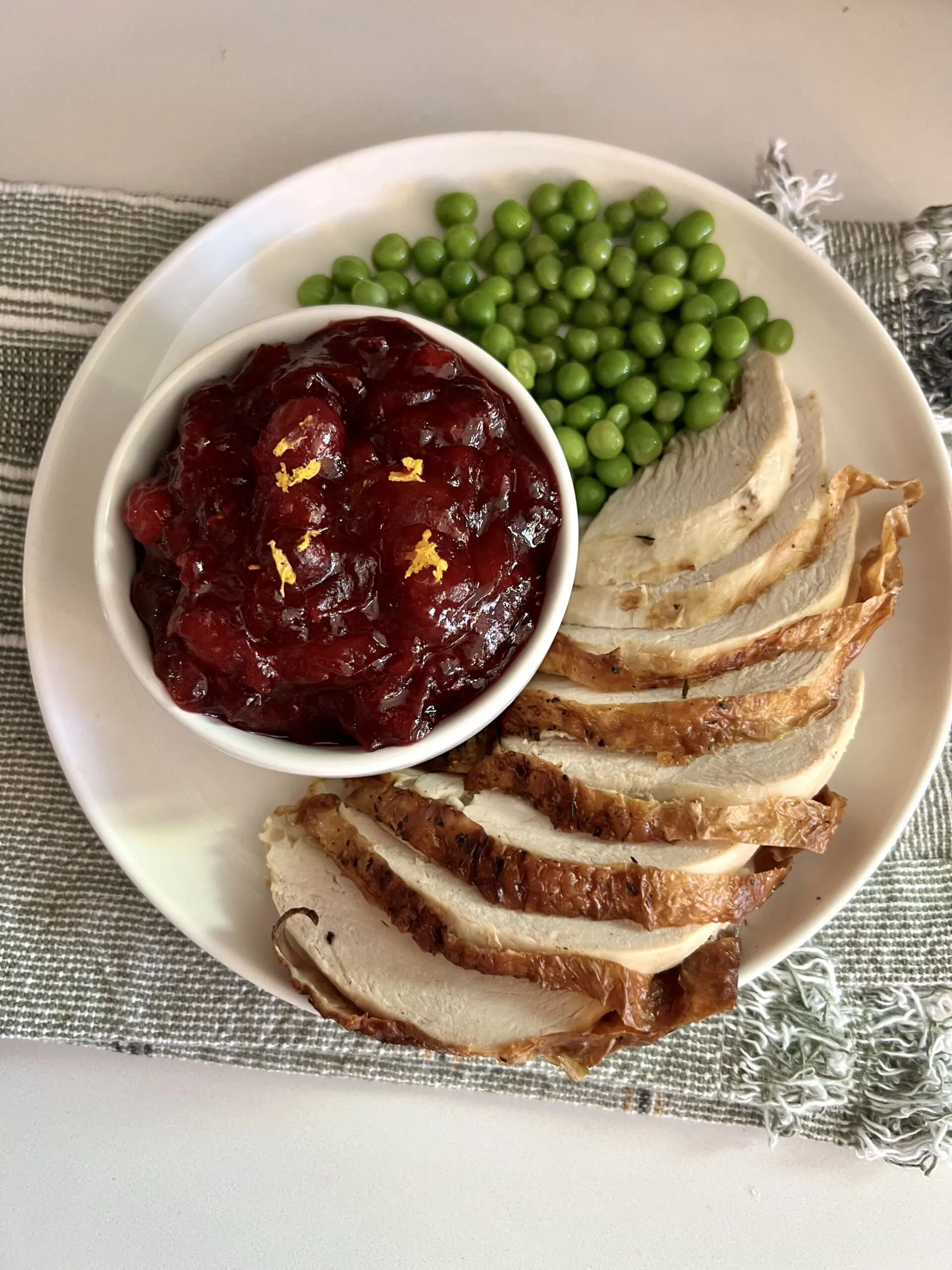 easy homemade cranberry sauce in a bowl next to turkey and peas on a white plate